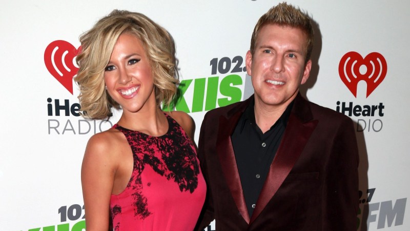 Savannah Chrisley, in a pink dress, stands with her father Todd, in a burgundy suit jacket, on the red carpet
