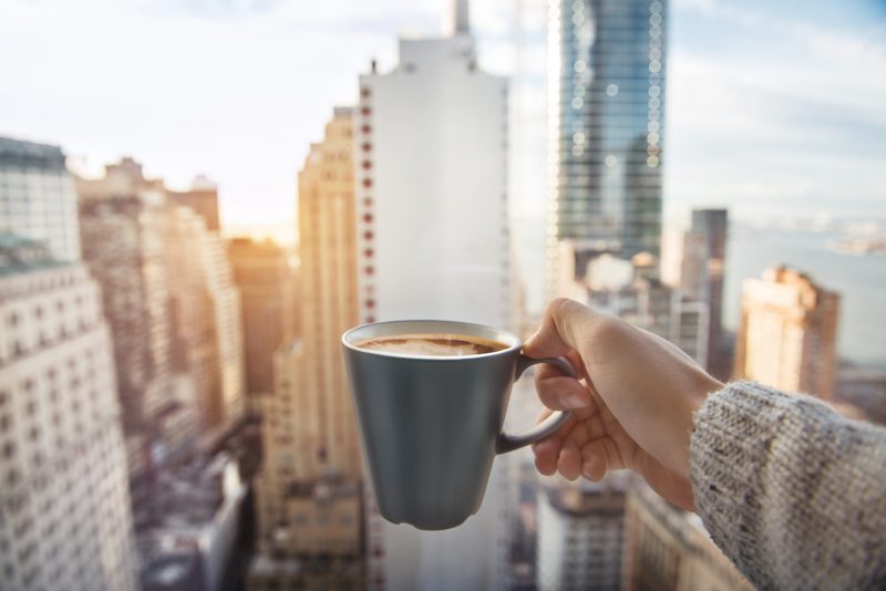 Image of person holding a mug in front of city.
