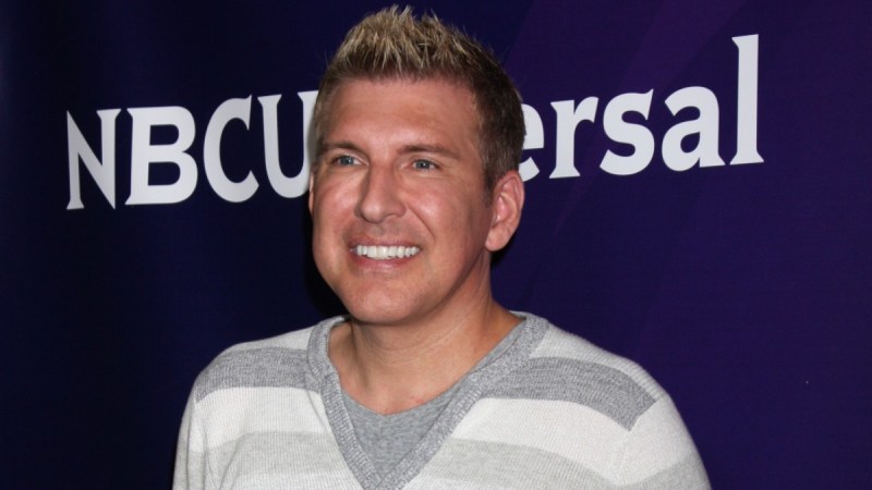Todd Chrisley wears a gray striped shirt against a blue background on the red carpet