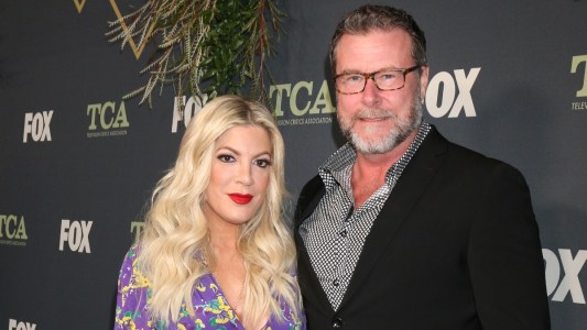 Tori Spelling, in a purple floral gown, stands with Dean McDermott, in a dark suit, on the red carpet