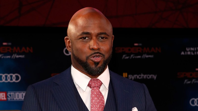 Wayne Brady wears a dark suit against a mostly black background