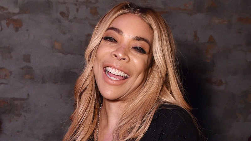 Wendy Williams laughs at the camera while wearing a black top and jean shorts