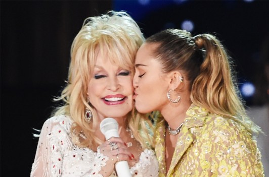 miley cyrus kissing dolly parton on the cheek during a performance
