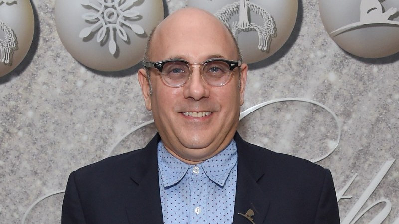 Willie Garson wears a blue shirt and dark suit jacket against a gray background