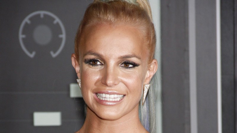 Britney Spears wears a gold dress and smiles big for the camera on the red carpet