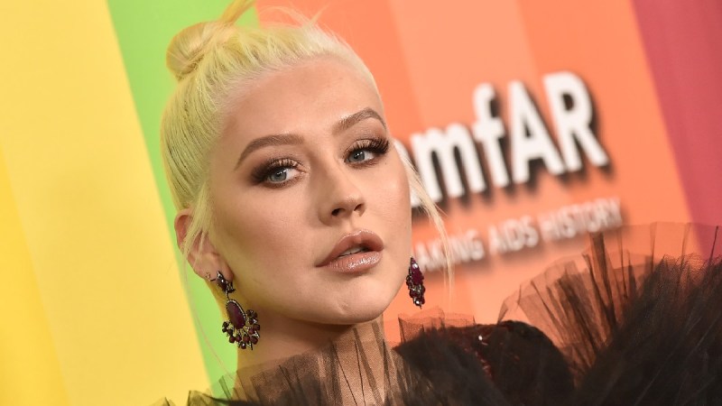 Christina Aguilera wears a large black dress against a multi-colored background