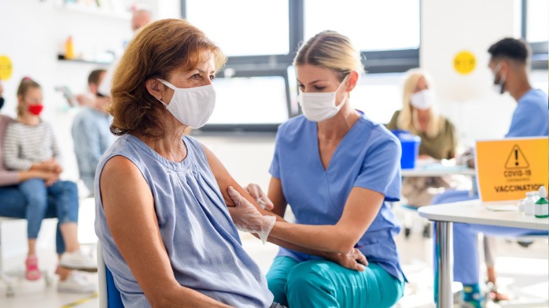 A woman in a blue top gets an injection from a woman wearing scrubs