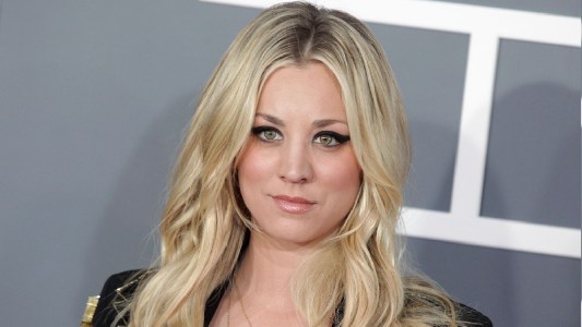 Kaley Cuoco wears a black jacket against a gray background on the red carpet