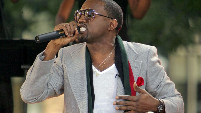 Kanye West wears a gray blazer over a white shirt as he performs onstage