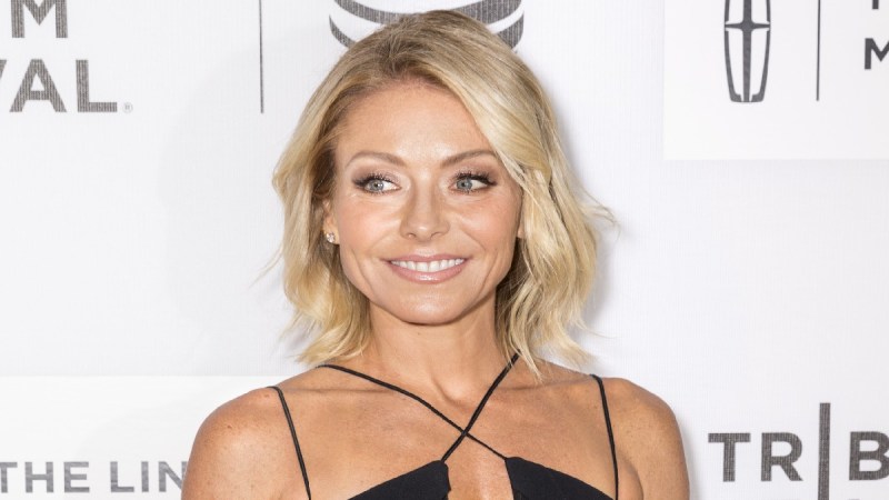 Kelly Ripa wears a black dress against a white background on the red carpet