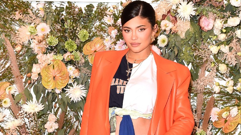 Kylie Jenner wear an orange jacket against a floral background