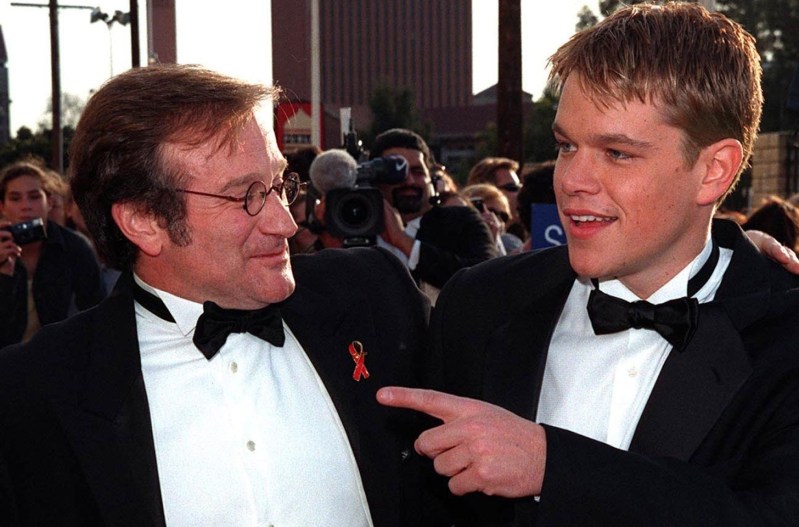 A young Matt Damon on the right, pointing at Robin Williams on the left, together at a red carpet event.