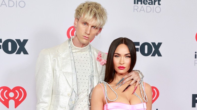 Machine Gun Kelly wears a white outfit and poses with Megan Fox, in a pink jumpsuit, on the red carpet