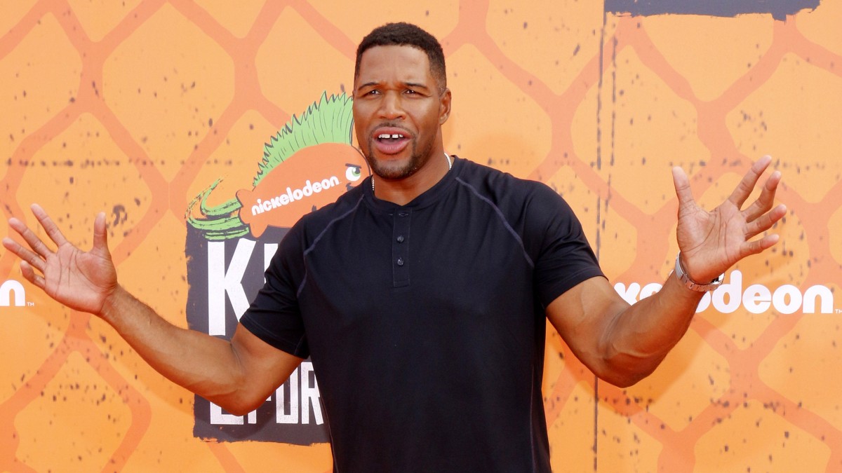 Michael Strahan wears a black shirt against an orange background