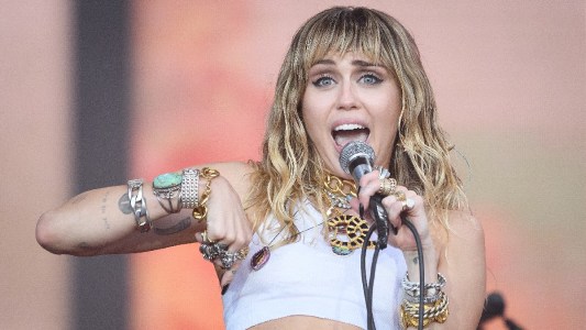 Miley Cyrus wears a white crop top and sings onstage during an outdoor performance