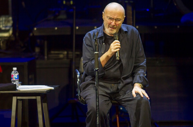 Phil Collins performing, seated, on stage.