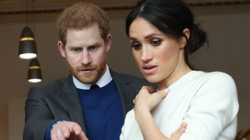 Prince Harry points at a prosthetic limb as Meghan Markle looks on