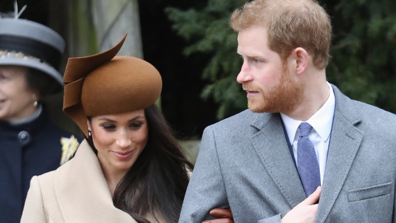 Meghan Markle wears a tan coat and walks with Prince Harry, in a gray coat