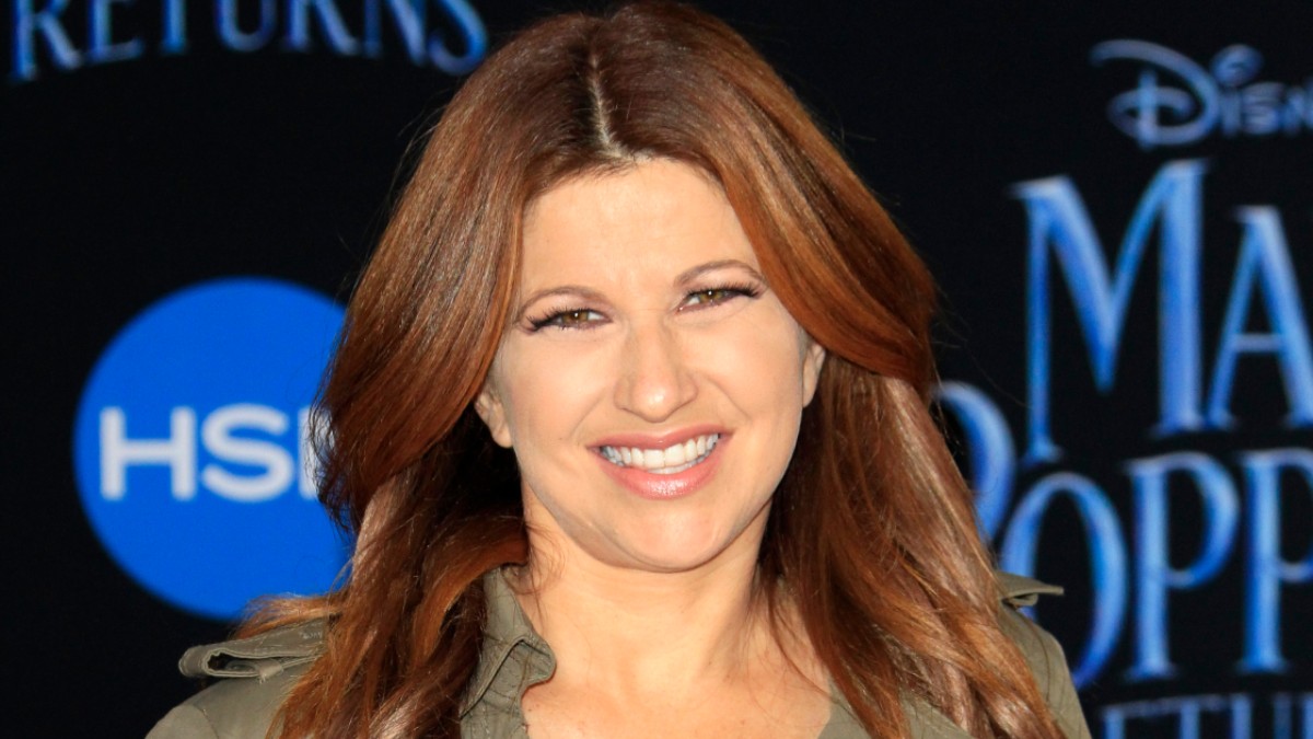 Rachel Nichols wears a tan jacket against a dark backdrop on the red carpet