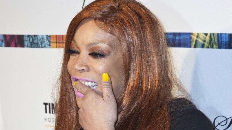 Wendy Williams uses a finger to scrub her teeth while wearing a black dress on the red carpet