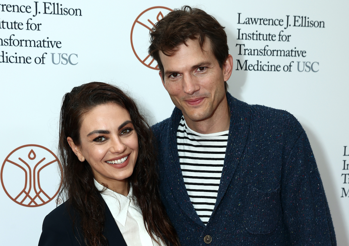 Mila Kunis in a white shirt and black coat and Ashton Kutcher in a blue cardigan