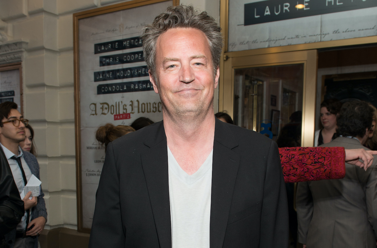 Matthew Perry smiling in a white shirt and black coat