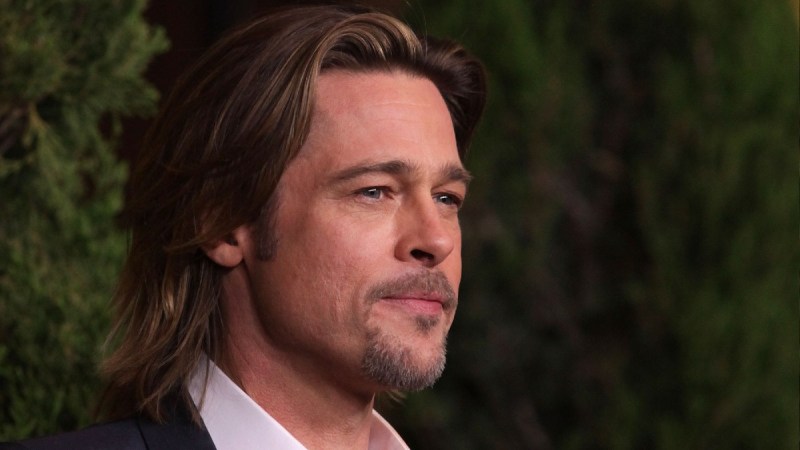Brad Pitt wears a dark suit as he walks the red carpet against a green background
