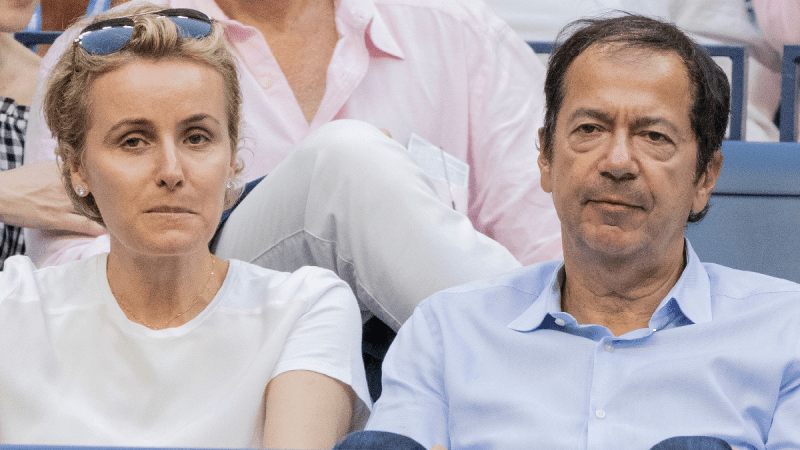 Jenny and John Paulson wear casual clothes while seated in the audience at a tennis match