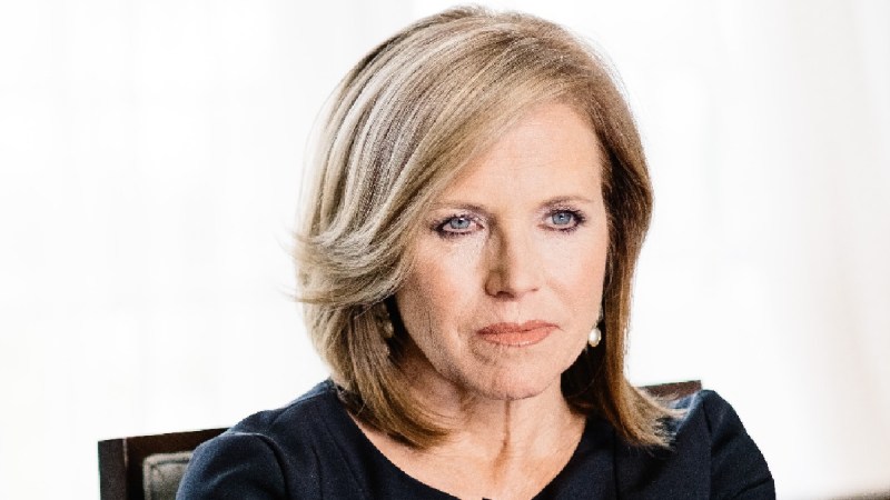 Katie Couric wears a black dress against a white background