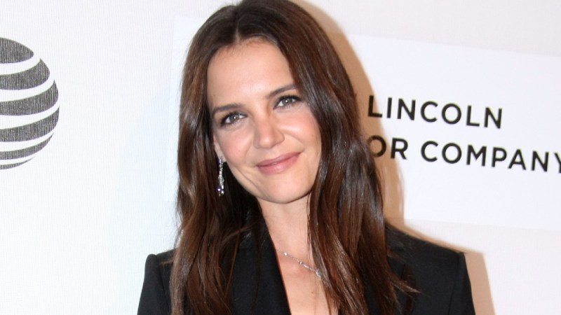 Katie Holmes wears a black suit against a white background on the red carpet