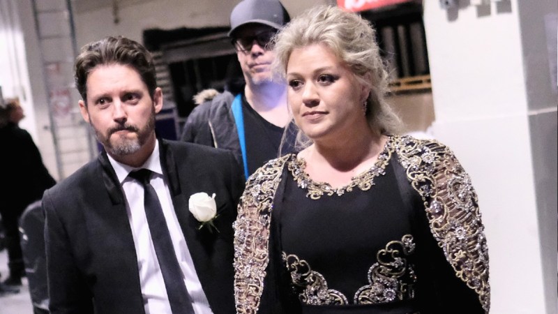 Brandon Blackstock, in a black suit, and Kelly Clarkson, in a black dress, walk together towards an awards event