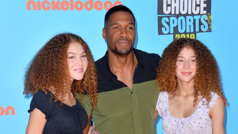 Michael Strahan, in a green shirt, poses with daughters Sophia and Isabella in front of a blue background