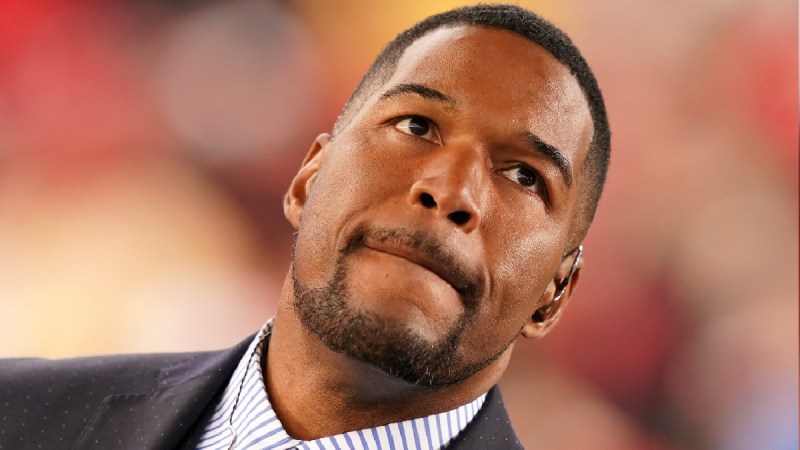Michael Strahan wears a dark suit at a football game