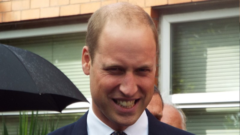 Prince William wears a dark suit and grins while walking the street