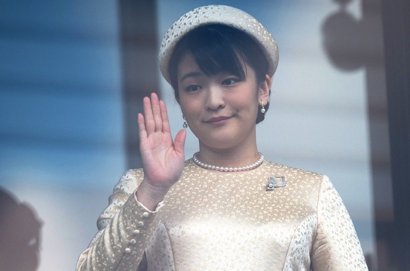 Princess Mako in a white dress and white hat, waving through a window.