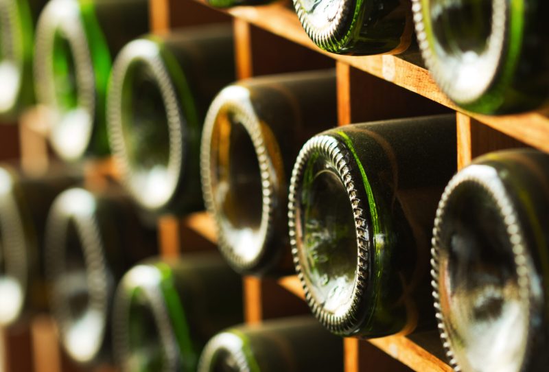 Bottom of wine bottles peeking out of a wooden cellar.
