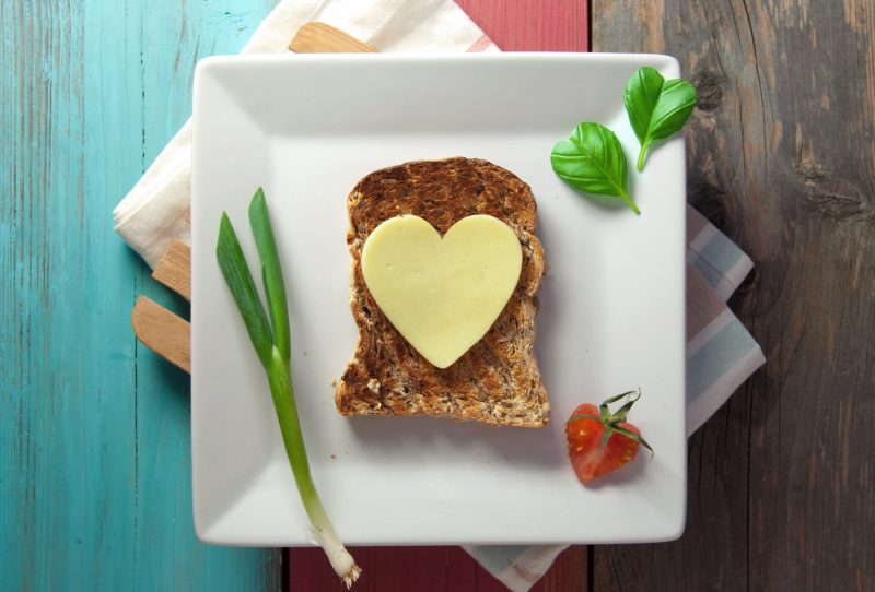Heart shaped cheese or butter on a piece of whole grain bread.