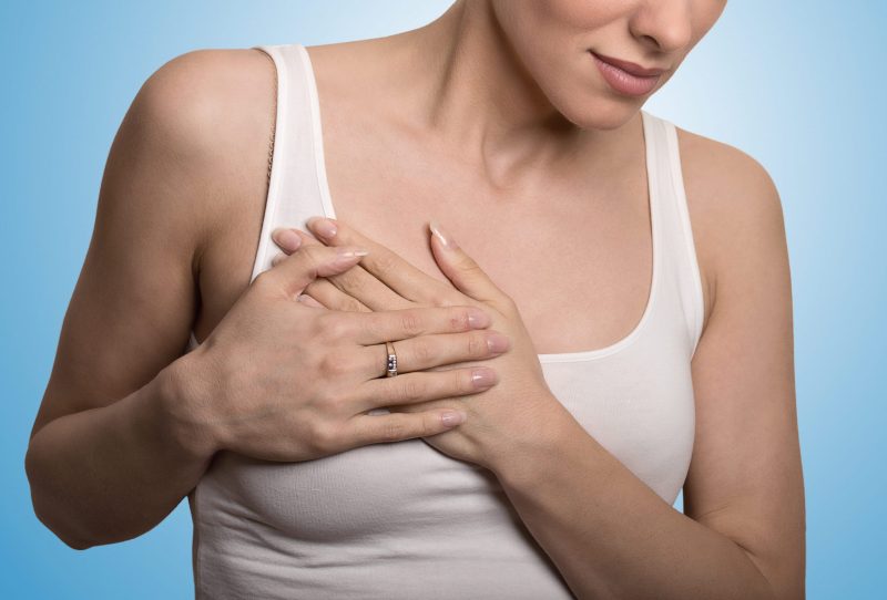 Woman touching chest with overlapped hands indicating breast pain.