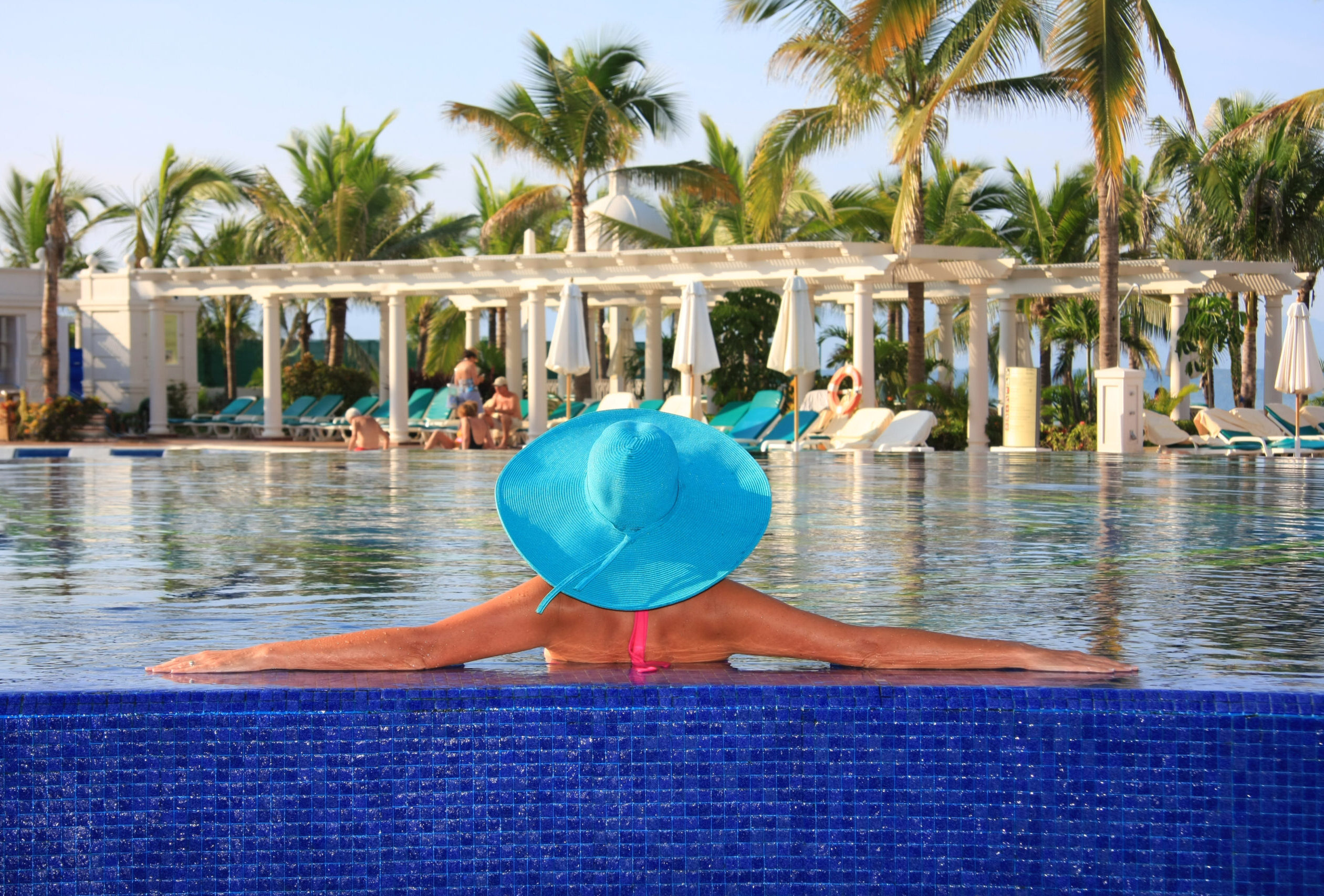 Woman in a sunhat relaxing in a pool at an all-inclusive resort.