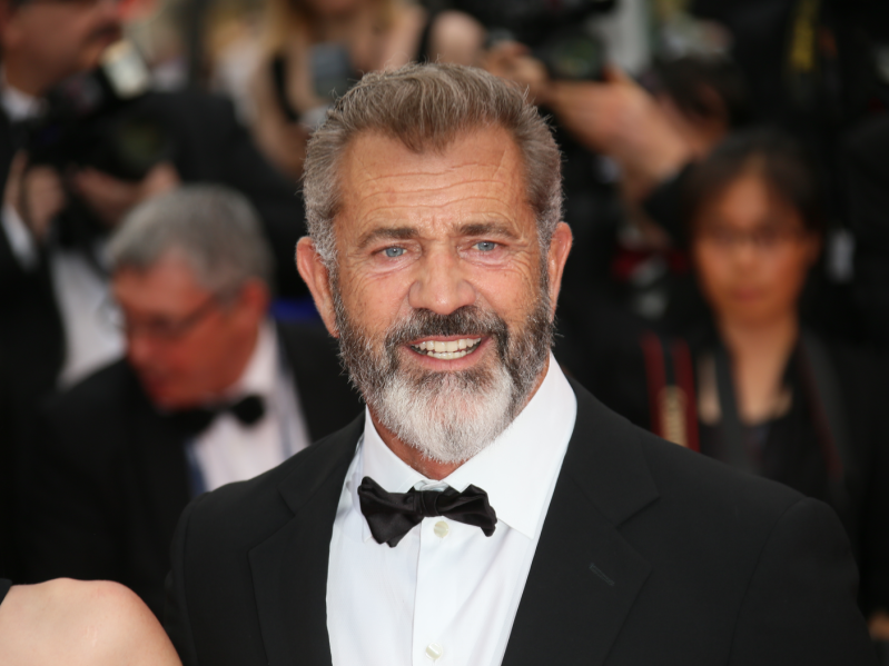 Mel Gibson smiles on the red carpet wearing a black tuxedo