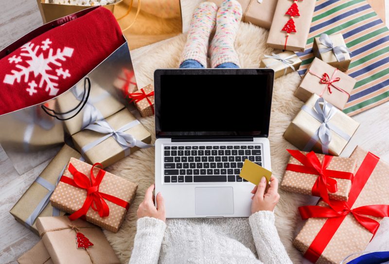 Woman with a laptop surrounded by wrapped holiday gifts.
