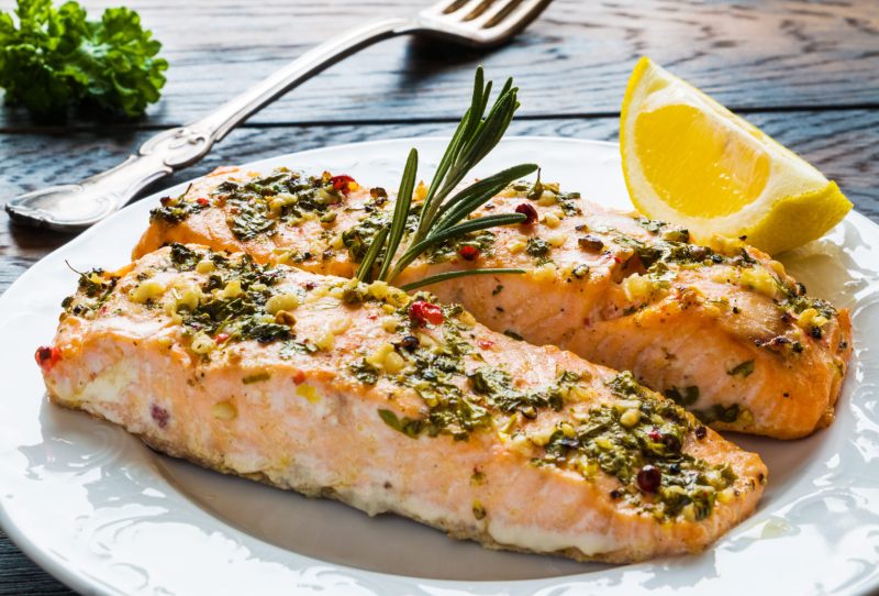 Cooked salmon on a plate with herbs and a lemon slice.