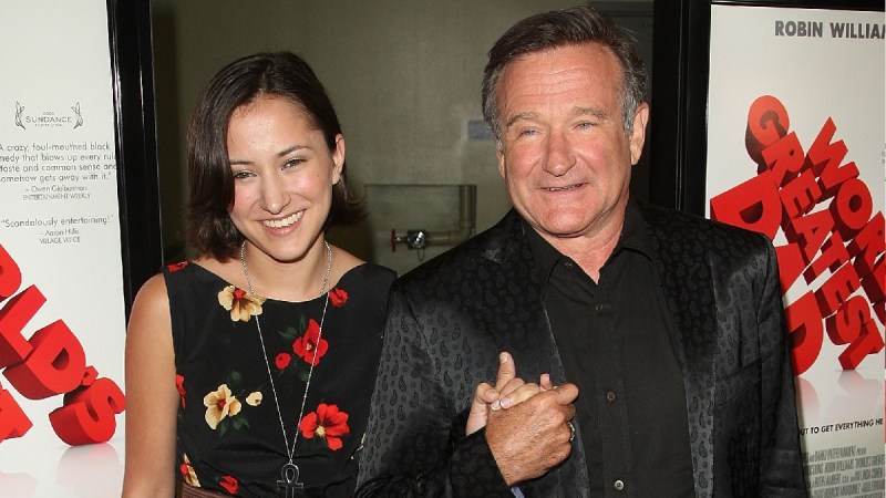 Zelda Williams, in a black dress with colorful flowers stands with Robin Williams, in a black suit, on the red carpet