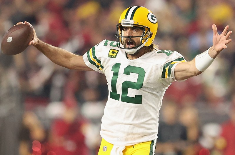 Aaron Rodgers on the field, looking frustrated with his arms out, holding a football