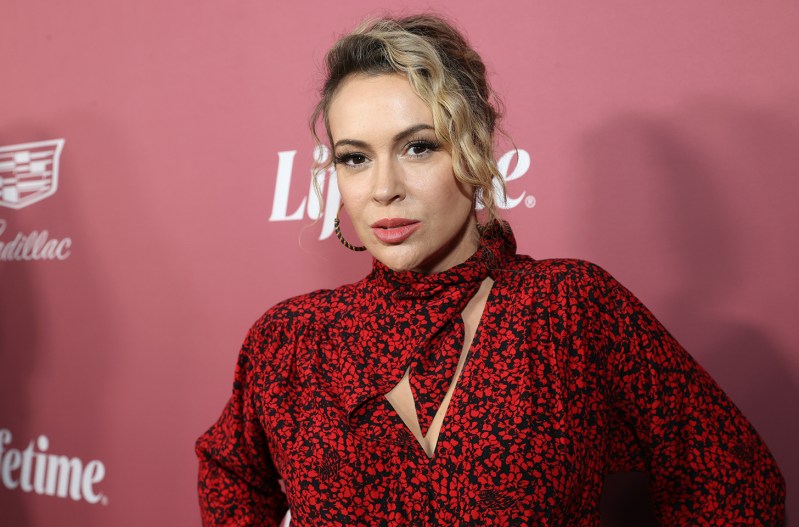 Alissa Milano looking serious, in a red dress at a red carpet event.
