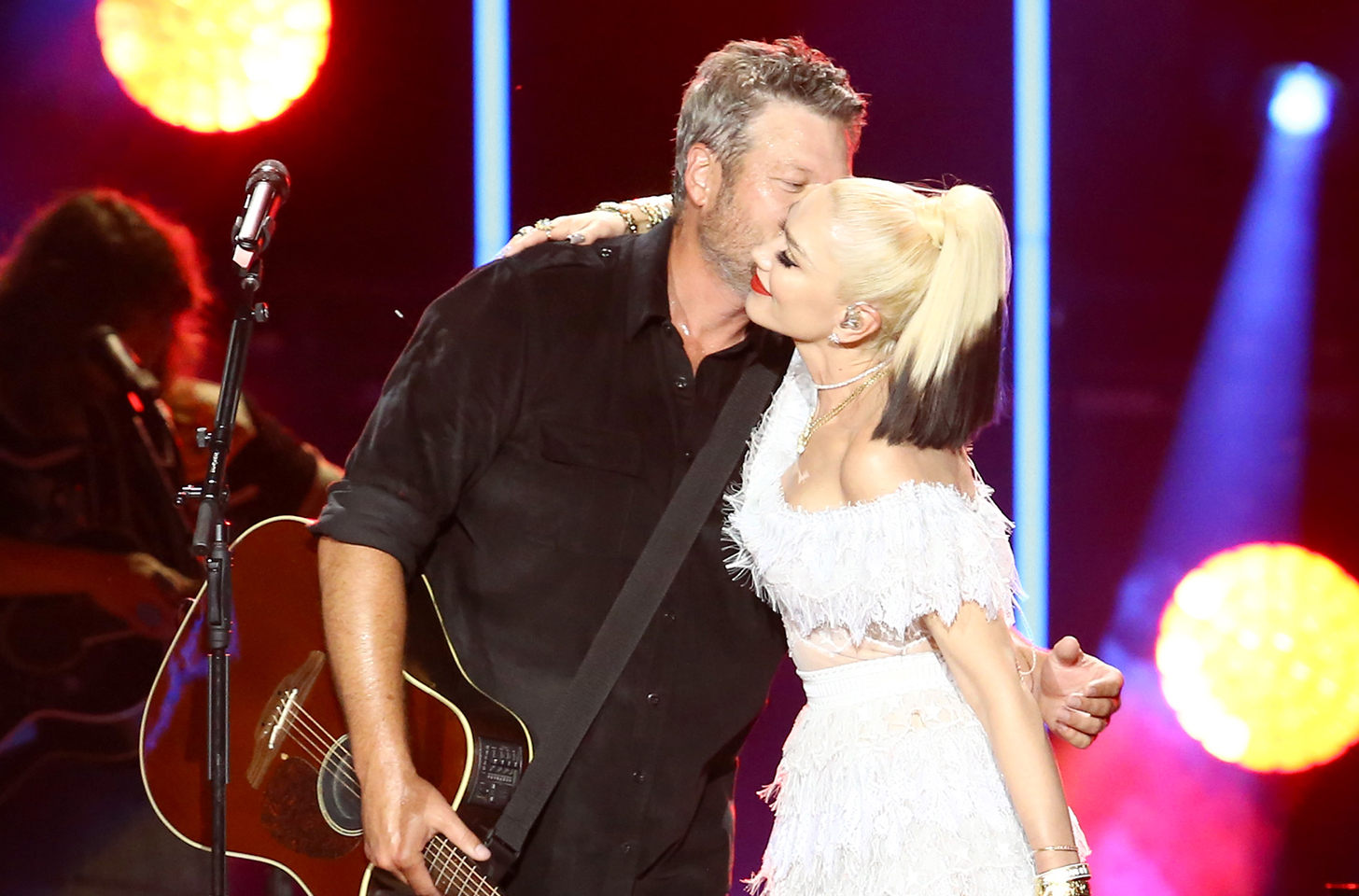 Blake Shelton kissing Gwen Stefani on the cheek on stage at a concert