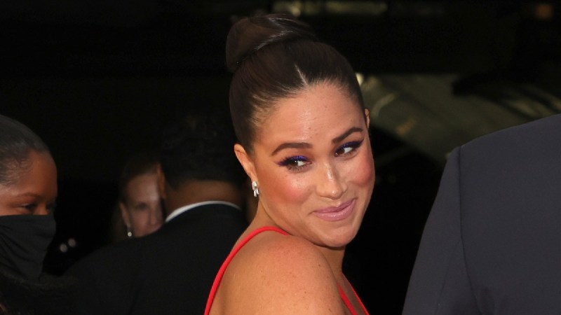 Meghan Markle wears a red dress and looks over her shoulder while attending an event with husband Prince Harry