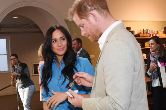 Meghan Markle smiling at Prince Harry as he tastes some food.