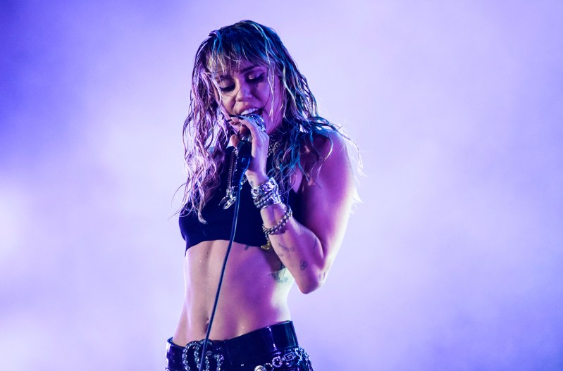 Miley Cyrus with a bare midriff performing on stage