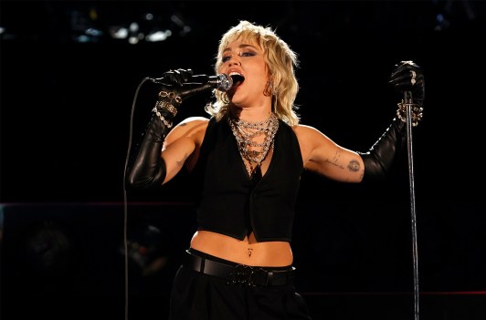 Miley Cyrus performing on stage in a black cut off shirt and black pants.